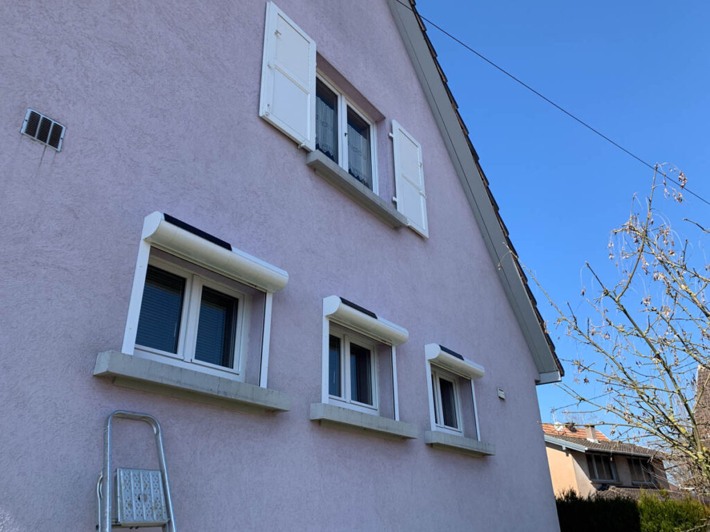Façade crépie équipée de fenêtres blanches et de volets roulants solaires à coffre extérieur